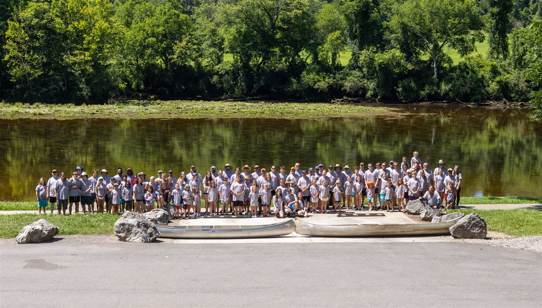 Fathers, children, and volunteers gathered beside the river behind two f3TCh canoes at Camp f3TCh 2026